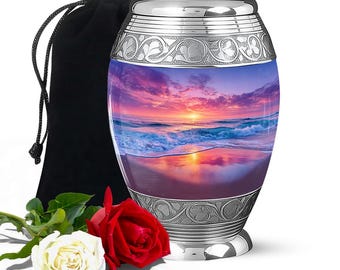 May include: A silver urn with a sunset scene, featuring a vibrant sky and ocean waves. The urn has decorative silver bands and is accompanied by a black velvet bag and two roses, one red and one white.