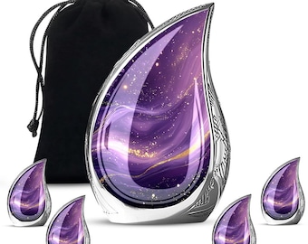 Puede incluir: Una urna en forma de lágrima con un diseño de galaxia en tonos morados y dorados, con un borde decorativo plateado. Incluye una bolsa negra con cordón y cuatro pequeños recuerdos a juego en forma de lágrima.