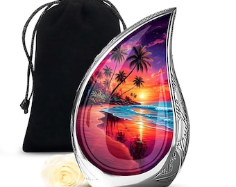 Puede incluir: Una urna conmemorativa plateada en forma de lágrima con una vibrante escena de playa al atardecer. La urna tiene un borde decorativo y una bolsa negra con cordón. Una rosa blanca se coloca cerca de la urna.