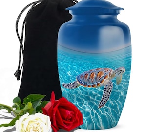 May include: A blue urn with a sea turtle design. The urn has a lid and is accompanied by a black velvet bag and two roses, one red and one white. The sea turtle is swimming in blue water.