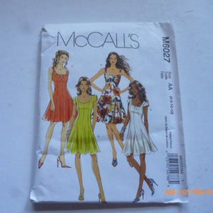 May include: A McCall's sewing pattern envelope featuring illustrations of four different dresses. The dresses are in red, green, floral, and white. The envelope has the McCall's logo and pattern number M6027.
