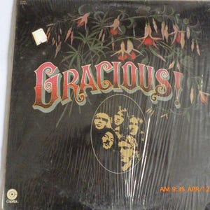 May include: A black vinyl record album cover with the title "Gracious!" in red and white lettering. The cover features a floral design and a group of people in a black and white photo.