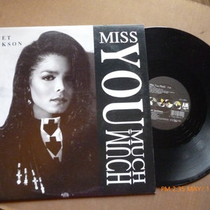 May include: A vinyl record album featuring Janet Jackson. The album cover is black and white, with a portrait of Jackson and the text "MISS YOU MUCH". The record itself is black and shiny.