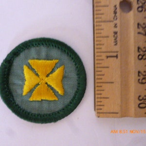 May include: A green and yellow embroidered patch with a four-pointed star design. The star is yellow and the background is green.