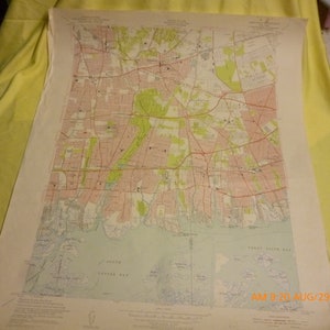 May include: A detailed topographic map with a coastal area, featuring roads, buildings, and green spaces. The map is printed on aged paper and includes text at the bottom. The map is resting on a yellow surface.