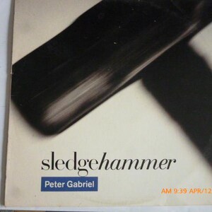 May include: Album cover for "Sledgehammer" by Peter Gabriel. The cover features a black, abstract design against a cream background. The title "sledgehammer" is in a stylized font, with the artist's name below in a blue box.