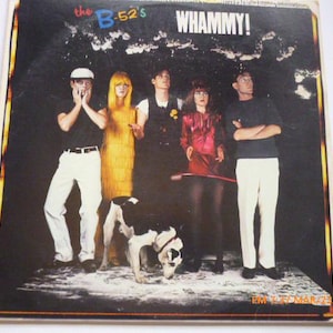 May include: Album cover for The B-52's "Whammy!" featuring the band members and a dog. The cover has a dark background with the band members in various outfits. The album title is in large, bold letters at the top.