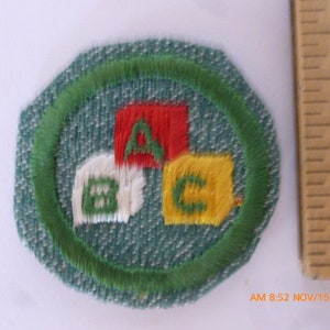 May include: A green fabric patch with a white border and a green circle in the center. Inside the circle are three embroidered blocks with the letters A, B, and C in different colors.