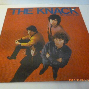 May include: A vinyl record album cover featuring a band called "The Knack" with the album title "Get The Knack" in blue text. The cover features four men in a band, with a red background.