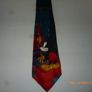 May include: A navy blue tie featuring a cartoon character design with red, yellow, and white accents. The tie has a red bottom and a dark blue top with a cartoon character design.