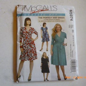 May include: McCall's Classic Fit sewing pattern for a knit dress. The pattern features illustrations of dresses in various styles, including a red and white floral print wrap dress, a blue floral dress, a teal wrap dress, and a black dress.