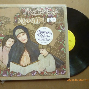 May include: A vinyl record album titled "Novella" by Renaissance. The album cover features an illustration of a woman in a black cloak with two children. The album is in its original packaging and includes a sticker that says "Renaissance featuring 'Midas Man'."