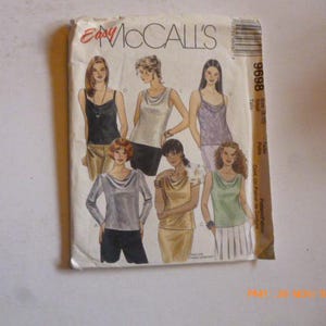 May include: A vintage sewing pattern from Easy McCall's featuring illustrations of various cowl-neck tops. The pattern packet displays images of tops in black, silver, gold, and green. The pattern number is 8696.