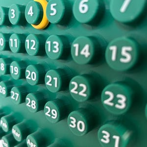 May include: A green wall calendar featuring raised circular buttons for each day of the month, numbered 3 through 31 in white text. A yellow ring highlights the number 4. Below the days, month abbreviations including Feb, Mar, Apr, May, and Dec are visible.