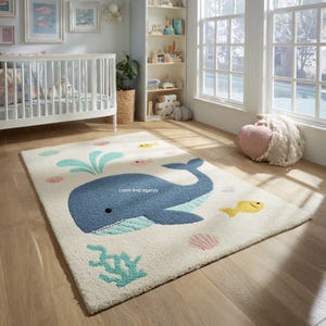 Pode incluir: Tapete retangular branco sujo com um design de baleia azul, jatos de água turquesa, peixes amarelos e detalhes de coral. O tapete está sobre um chão de madeira, ideal para um quarto infantil.