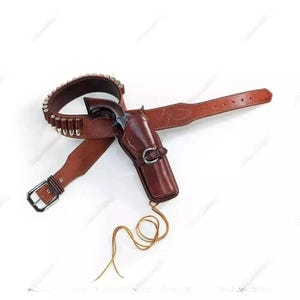 Könnte beinhalten: Ein brauner Leder-Gürtel mit einer Pistolenholster und einem Revolver. Der Gürtel ist mit Patronenschlaufen und einer silbernen Schnalle verziert. Das Holster ist dunkler braun und hat einen silbernen Verschluss. Eine goldfarbene Schnur hängt vom Holster.