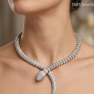 Puede incluir: Un collar con forma de serpiente en tono plateado con un diseño texturizado de escamas incrustado con numerosas piedras pequeñas, claras y brillantes. La pieza rodea el cuello con la cabeza de la serpiente en el centro. Texto: D&S Jewellers.