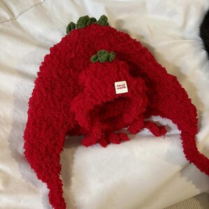 May include: A red, plush hat and matching scarf set. The hat has a small green accent on top, and the scarf has a long, flowing design. The set includes a small tag that reads "hand made".