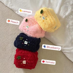 May include: Four fluffy, handmade, fruit-themed pouches in yellow, pink, navy blue, and red. Each pouch has a small green leaf accent and a tag that says "hand made". The pouches are labeled "Lemon", "Peach", "Blueberry", and "Tomato".