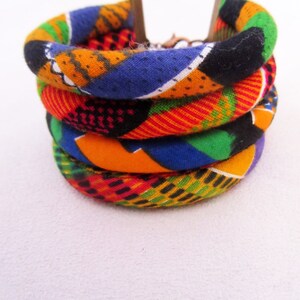 May include: A stack of four colourful fabric bracelets with a geometric pattern in shades of orange, green, blue, red and black.
