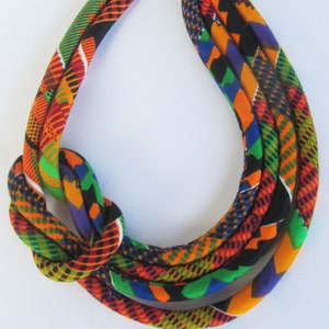 May include: A colourful fabric necklace with a knotted design. The necklace is made of multiple strands of fabric in shades of orange, green, blue, and black.