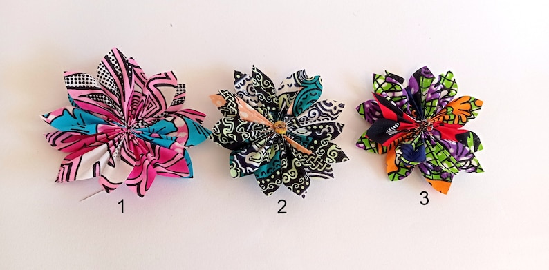 May include: Three fabric flower hair clips in different patterns. The first clip is pink, blue, and white. The second clip is black, green, and white. The third clip is red, green, purple, and orange.