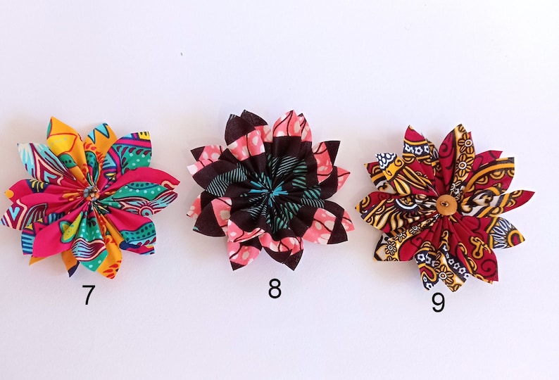 May include: Three fabric flowers with colorful patterns. The flowers are pink, red, and black with yellow accents. The flowers are numbered 7, 8, and 9.
