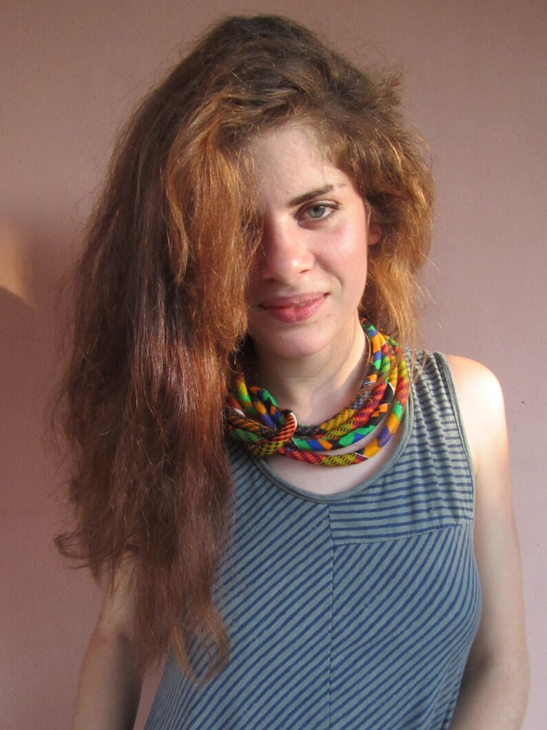 May include: A woman with long brown hair wearing a blue and white striped tank top with a colourful woven necklace.