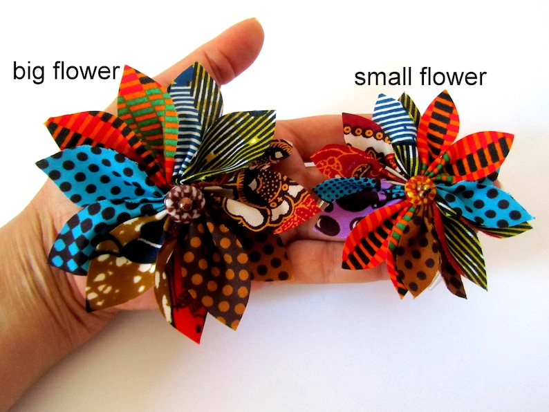 May include: Two fabric flowers, one large and one small, with a variety of colorful patterns and a brown button center. The flowers are made from African wax print fabric.