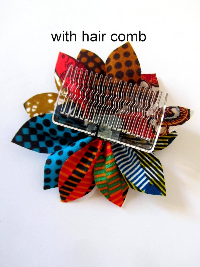 May include: A colorful fabric flower hair clip with a clear plastic comb attached. The flower is made of multiple fabric petals in various patterns, including polka dots, stripes, and geometric designs. The colors include red, orange, yellow, green, blue, and black.