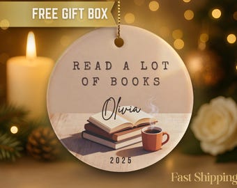 May include: A round, cream-colored ornament with the text "READ A LOT OF BOOKS" and the name "Olivia." It features a stack of books, a mug of coffee, and the year 2025. A gift box is shown at the top.