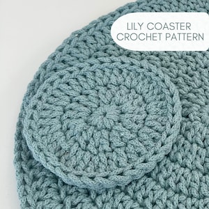 May include: A close-up of a crocheted coaster and placemat set in a soft blue-green colour. The coaster is round, and the placemat is partially visible, with the text "LILY COASTER CROCHET PATTERN" in a white oval.