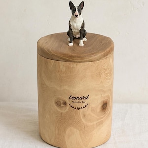 Puede incluir: Una urna cil&iacute;ndrica de madera con veta marr&oacute;n claro natural y tapa extra&iacute;ble. Una peque&ntilde;a figura pintada a mano de un Bull Terrier blanco y negro se asienta en la parte superior. El frente est&aacute; grabado con el texto Leonard Always Our Boy y un coraz&oacute;n.