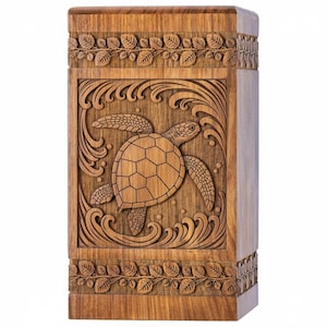 Pode incluir: Urna de madeira com um design entalhado de tartaruga marinha. A tartaruga é cercada por ondas e emoldurada por padrões decorativos de folhas. A urna é retangular e feita de madeira marrom claro.
