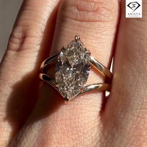 Op de afbeelding: Een verlovingsring met een marquise-geslepen diamant en een split-schachtband. De ring heeft een grote, heldere diamant gezet in een gouden band. De ring wordt op een vinger getoond en vangt het licht.
