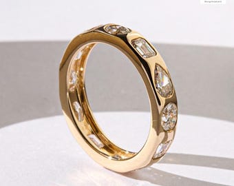May include: A gold ring with a series of various shaped diamonds. The ring features a mix of round, emerald, and pear-shaped diamonds set in a polished gold band. The ring is displayed on a white surface.