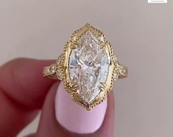 May include: A marquise-cut diamond ring with a gold band. The ring features an ornate, filigree-style setting with small accent stones. The diamond is the focal point, reflecting light. The ring is a piece of jewelry.