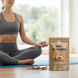 May include: A woman in gray activewear sits in a yoga pose next to a package of "Organic Ashwagandha" powder. The package is brown with the brand name "LIV FIT" and product details. Ashwagandha root pieces are in the foreground.