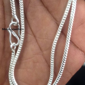 May include: A silver chain with a hook clasp, shown against a skin-toned background. The chain features a tightly woven, textured design. The text "Meenujewellers" is visible.