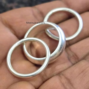 以下が含まれることがあります： 3つのシルバーリングが、その円形デザインを強調して表示されています。 リングは滑らかで光沢のある表面を持ち、光を反射しています。 リングは積み重ねられています。 「Meenujewellers」の文字が見えます。