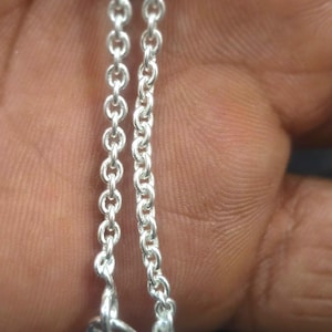 May include: Close-up of two silver chain necklaces. The chains are made of small, interconnected links. The text "Meenujewellers" is visible in the upper left corner. The chains are displayed against a skin-toned background.