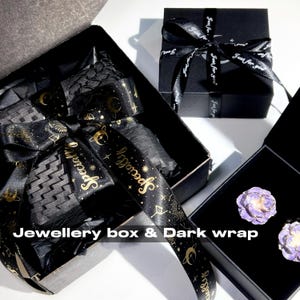 May include: Black jewelry boxes with black ribbon and gold text. One box is open, revealing black tissue paper and a decorative ribbon. Another box is closed with a ribbon that says "Just for you". The text "Jewellery box & Dark wrap" is visible.