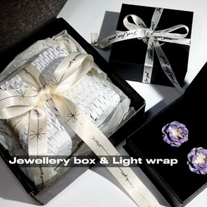 May include: Black jewelry boxes with white ribbon and the text "Just for you". One box is open, revealing white packaging and a cream ribbon with the text "thank you". Two purple flower earrings are in another box. The text "Jewellery box & Light wrap" is visible.