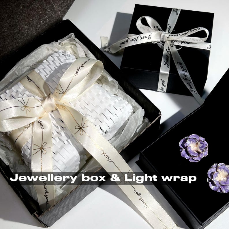 May include: Black jewelry boxes with white ribbon and the text "Just for you". One box is open, revealing white packaging and a cream ribbon with the text "thank you". Two purple flower earrings are in another box. The text "Jewellery box & Light wrap" is visible.