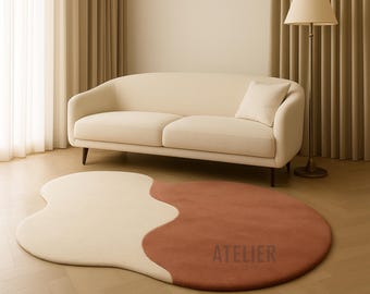 Könnte beinhalten: Zweifarbiges Teppich mit organischer Form in Creme und Rost. Auf dem rostfarbenen Bereich ist das Wort "ATELIER" aufgedruckt. Im Hintergrund befinden sich ein cremefarbenes Sofa und eine Lampe. Ein stilvolles Wohnaccessoire.