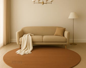 Puede incluir: Una alfombra redonda de color óxido domina el primer plano, con la palabra "ATELIER" impresa en ella. Un sofá beige con una manta y un cojín a juego se encuentra contra una pared neutra. Una lámpara de araña y una lámpara de pie doradas completan la decoración de la habitación.