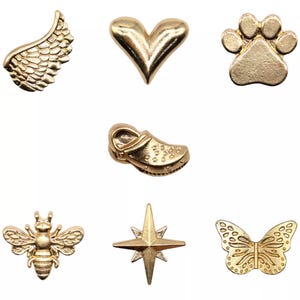 May include: A selection of gold-coloured charms in diverse shapes: a wing, heart, paw print, clog, bee, star, and butterfly. These small, detailed charms are likely for jewellery making or craft projects.