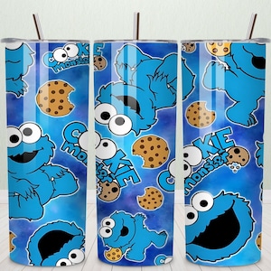 Puede incluir: Tres vasos de acero inoxidable con un fondo azul con el Monstruo de las Galletas y galletas. Las palabras "Cookie Monster" están impresas en los vasos. Cada vaso tiene una pajita.