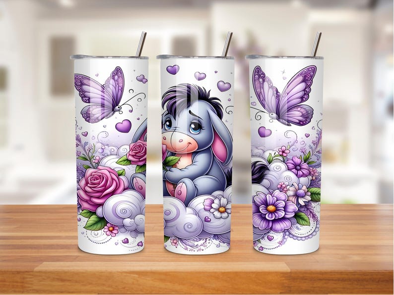 May include: Three white stainless steel tumblers with illustrations of a cartoon donkey, butterflies, flowers, and clouds. The tumblers have silver straws and lids. The design features purple, pink, and white colours.