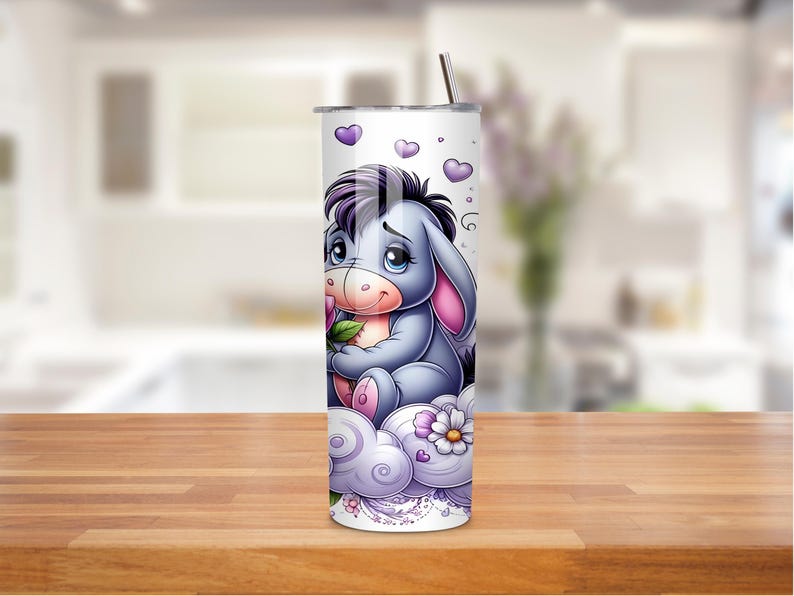 May include: A white tumbler with a cartoon donkey character in purple and grey. The donkey is sitting on a cloud with flowers and hearts. A silver straw is inserted into the top of the tumbler.